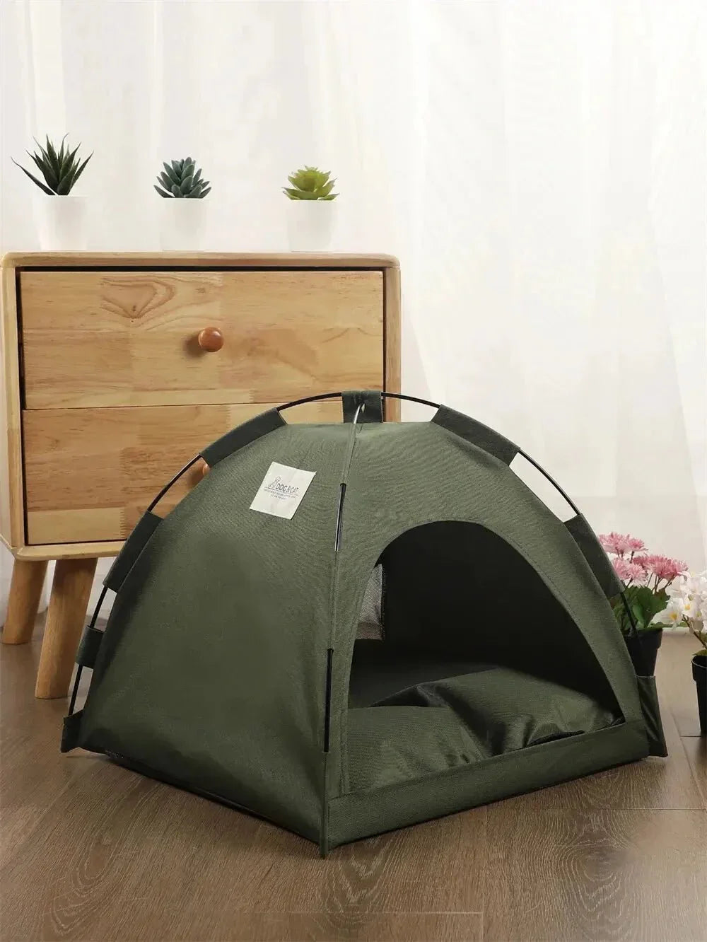 Green cat tent bed on wooden floor with nightstand and potted plants nearby
