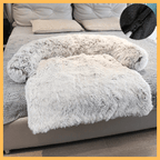 Comfy Shield plush pet blanket in light gray on a bed, featuring anti-slip bottom detail.