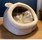 Fluffy white cat lounging in a soft bunny-ear cat bed with pompom toy indoors