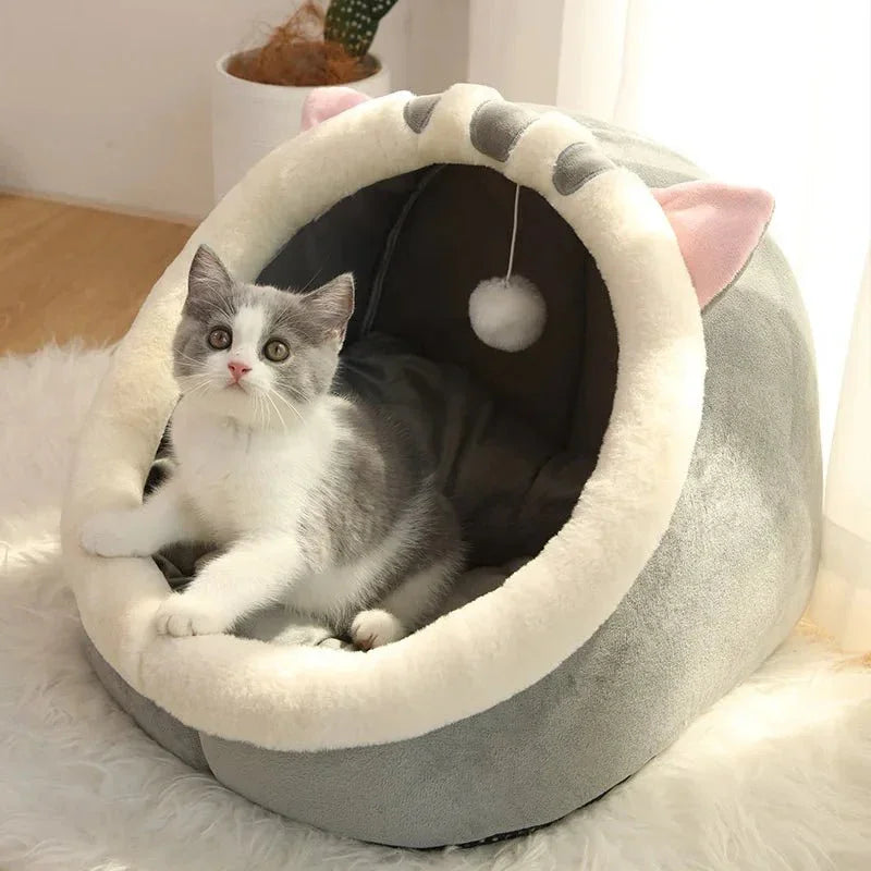 Gray and white cat in a cozy plush cat cave bed with ears and a hanging toy ball