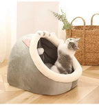 Gray and white cat in cozy plush cat cave bed on wooden floor with basket in background