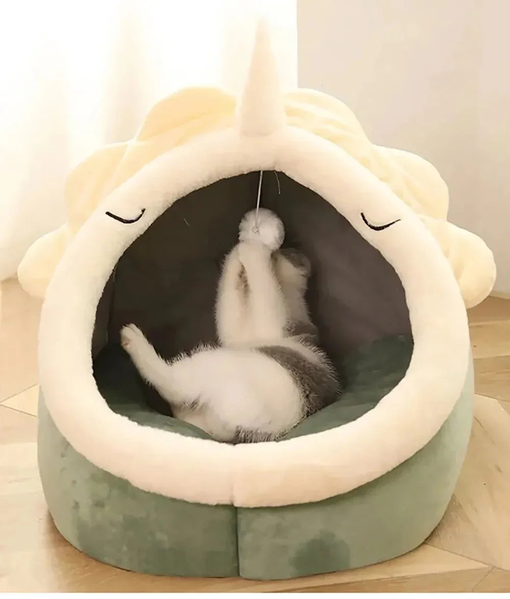 Kitten playing inside plush unicorn cat cave bed with ball toy on wooden floor