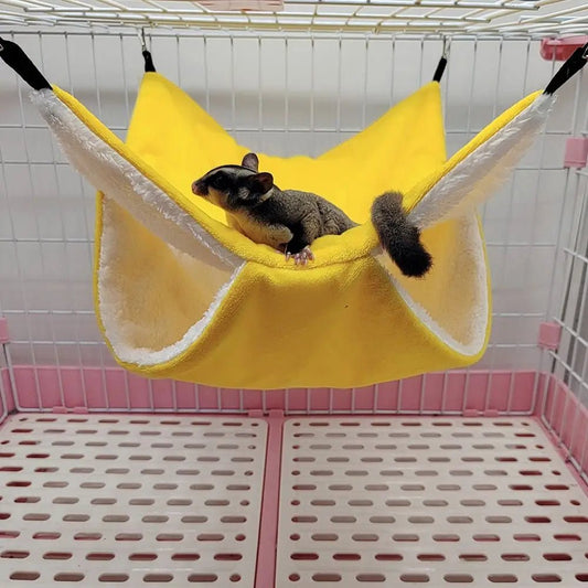 Sugar glider resting in a yellow fleece hammock inside a white wire pet cage