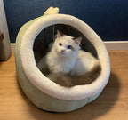 White fluffy cat sitting in a cozy plush cat bed on wooden floor indoors