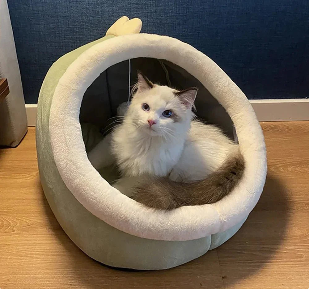White fluffy cat sitting in a cozy plush cat bed on wooden floor indoors