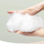 Hands holding soft, fluffy white cotton fiber against a light background