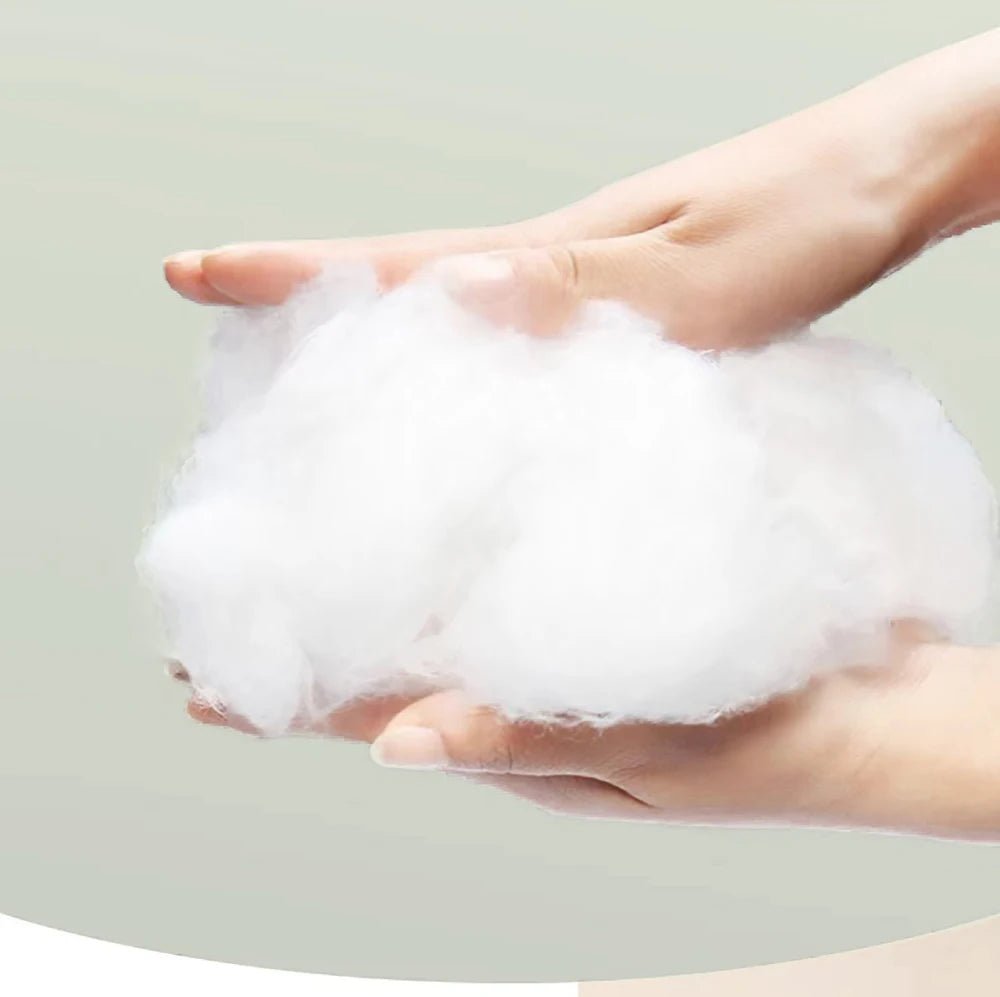 Hands holding soft, fluffy white cotton fiber against a light background