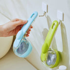 Hand holding blue pet bath brush beside green bath brush on wall hooks in bathroom.