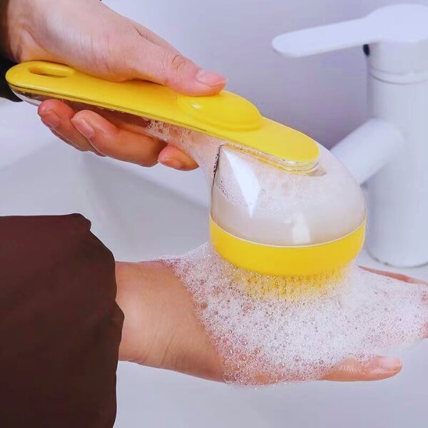 Hand using yellow pet bath brush with foam by sink, grooming tool for dogs and cats