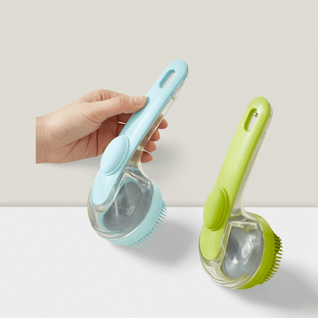 Blue and green pet bath brushes with silicone bristles on a table, one held by a hand.