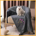 Fluffy white cat on gray pet blanket with heart and dog design, cozy chair by window