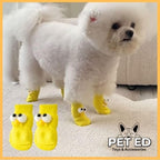Small white dog wearing yellow non-slip dog socks with cartoon eyes on a carpet indoors