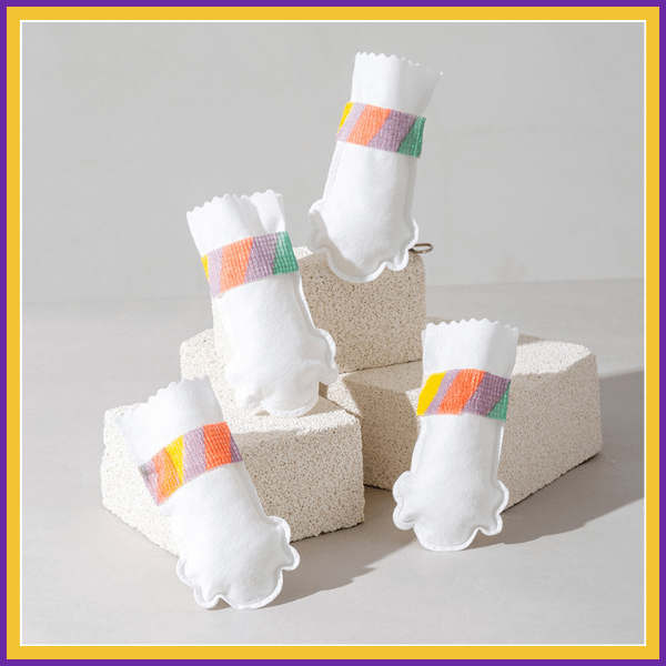 Four white Drypaws dog shoes with colorful bands displayed on light blocks