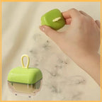 Hand using portable green Haarrol hair remover on fabric with visible hair