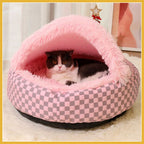 Cat resting in a pink plush hooded pet bed with checkered pattern indoors