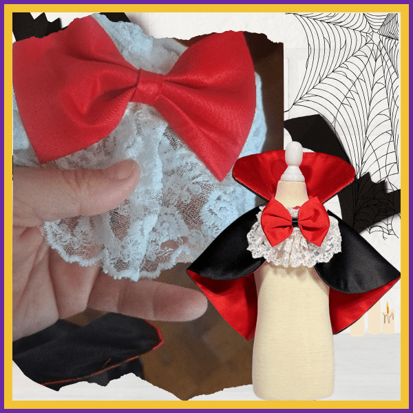 Close-up of a red bow and white lace ruffle beside a black and red vampire cape on a mannequin