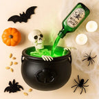 Black witches cauldron with a skeleton and green mist, surrounded by a pumpkin, bats and spiders for Halloween