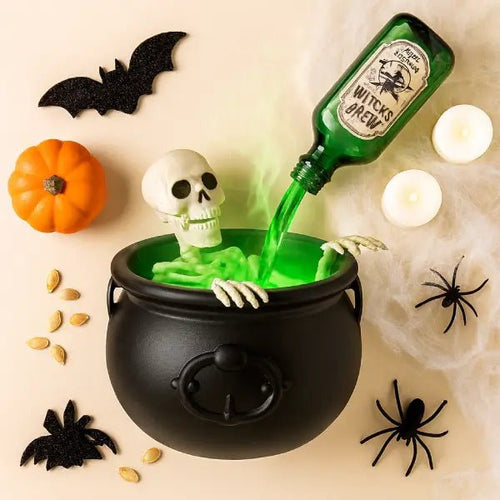 Black witches cauldron with a skeleton and green mist, surrounded by a pumpkin, bats and spiders for Halloween