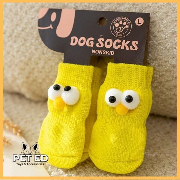 Yellow non-slip dog socks with cartoon eyes in retail packaging, PET ED logo visible