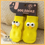 Yellow non-slip dog socks with cartoon eyes in retail packaging, PET ED logo visible